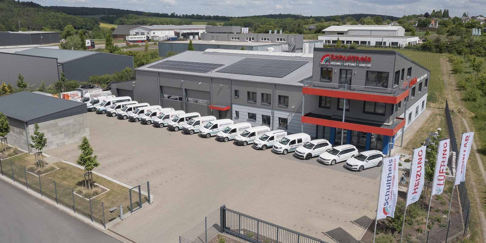 Das Firmengebäude mit dem Namen 'Schulthess' und mehreren Fahrzeugen, die für Dienstleistungen bereitstehen, in einer ländlichen Umgebung.