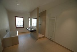 Ein modernes Badezimmer mit einer Badewanne, einem Waschbecken und einer Dusche, umgeben von hellen Wänden und Fenstern.