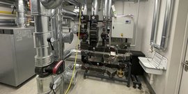Ein technischer Raum mit zahlreichen Rohren und Ventilen, die an einer Wand montiert sind, zeigt komplexe Heizungs- und Lüftungstechnik.