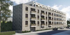 Die Fassade des Gebäudes zeigt Balkone mit Pflanzen, während Autos auf der Straße parken und der Himmel teilweise bewölkt ist.