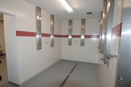 Der Umkleideraum zeigt eine helle, saubere Umgebung mit mehreren Duschstationen und einem grauen Bodenbelag.