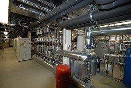 Die Innenansicht eines Maschinenraums, in dem metallische Rohre und ein roter Druckbehälter sichtbar sind.