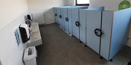 Ein gut gestalteter Sanitärbereich mit blauen Kabinen, modernen Waschbecken und einem Abfalleimer für Sauberkeit und Komfort.