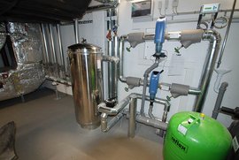 Die Installation zeigt eine komplexe Rohrleitung mit blauen und grauen Ventilen sowie einem grünen Druckbehälter.