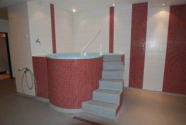 Ein moderner Wellnessbereich mit einem runden Whirlpool, umgeben von weißen Fliesen und roten Mosaikakzenten.