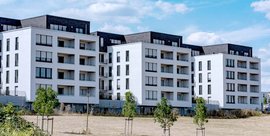 Moderne Wohngebäude mit weißen Fassaden und großen Fenstern, umgeben von einem offenen Feld und kleinen Bäumen.