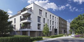 Moderne Wohnanlage mit hellen Fassaden, Balkonen und üppiger Begrünung, umgeben von einem klaren blauen Himmel.