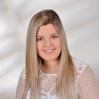 Porträt einer lächelnden Frau mit blonden Haaren Eine junge Frau mit langen, blonden Haaren lächelt freundlich in die Kamera, während sie ein weißes, durchscheinendes Oberteil trägt.