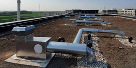 Eine Dachlandschaft mit silbernen Lüftungsrohren und einem großen Lüfter, umgeben von Kies und Gras.