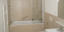 Das Badezimmer zeigt eine elegante Badewanne mit einer Glasduschabtrennung und einem großen Spiegel über dem Waschbecken.