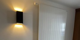 Die elegante schwarze Wandleuchte erzeugt sanfte Lichtstrahlen, die die Wand akzentuieren, neben einem weißen Heizkörper.