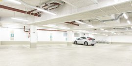 Der Innenraum eines modernen Parkhauses, in dem ein einzelnes Auto parkt, umgeben von leeren Stellplätzen.