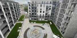 Ein moderner Innenhof mit gepflegtem Rasen und einem runden Brunnen, umgeben von eleganten Wohngebäuden.