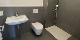 Ein modernes Badezimmer mit einer eleganten Wandtoilette und einem schlichten Waschbecken in neutralen Grautönen.