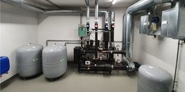 Ein technischer Raum mit mehreren großen grauen Druckbehältern und einem komplexen Rohrleitungssystem an der Wand.