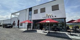 Ein modernes Restaurant mit dem Namen 'Riesen Friesen', das eine einladende Terrasse mit roten Sonnenschirmen bietet.