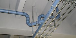 Ein komplexes Rohrsystem aus blauen Rohren, das an einer Decke befestigt ist, zeigt verschiedene Kurven und Verbindungen.