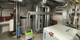 Ein technischer Raum mit mehreren großen silbernen Rohren und einem Heizgerät, das für die Energieversorgung genutzt wird.