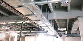 Die Decke eines modernen Raumes mit sichtbaren Lüftungsrohren und elektrischen Leitungen, die für eine industrielle Atmosphäre sorgen.