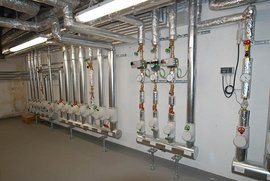 Eine Reihe von silbernen Rohren und Ventilen, die an einer Wand in einem technischen Raum installiert sind.