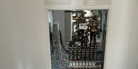 Das Bild zeigt eine komplexe Heizungsanlage mit verschiedenen Messgeräten und Ventilen, die ordentlich angeordnet sind.