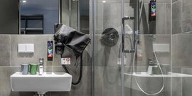 Ein modernes Badezimmer mit grauen Fliesen, einem Waschbecken und einem Haartrockner, der an der Wand hängt.