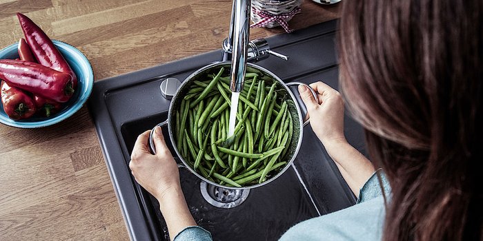 Eine Frau haelt ein Topf mit Bohnen unter der laufenden Kuechenspuehle 
