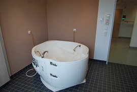 Ein modernes, weißes Whirlpool steht in einem hellen Raum mit braunen Wänden und grauem Bodenfliesen.