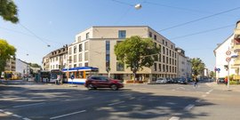 Eine belebte Straßenszene mit modernen Gebäuden, Straßenbahnen und Bussen, die unter blauem Himmel verkehren.