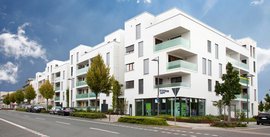 Eine Reihe eleganter, weißer Wohnhäuser mit Balkonen, die in einer städtischen Umgebung stehen, unter einem blauen Himmel.