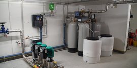 In einem Kellerraum sind mehrere Wasserbehälter und Pumpen sichtbar, die für die Wasserverteilung und -behandlung genutzt werden.