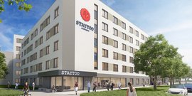 Das Gebäude 'STAYTOO' bietet eine freundliche Atmosphäre, während Passanten und Radfahrer die Umgebung genießen.