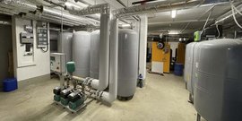 Ein Raum mit großen grauen Wassertanks, Rohren und einer Steuerungseinheit für die Wasseraufbereitung.