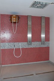 Ein modernes Duschbad mit rot gefliester Wand, zwei Edelstahl-Duschpaneelen und einem Holzfass für Wasser.
