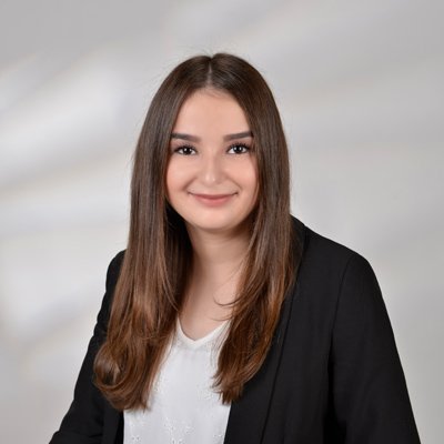 Eine junge Frau mit langen, glatten Haaren lächelt freundlich in die Kamera, gekleidet in einem schwarzen Blazer.