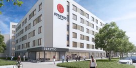 Die Fassade eines eleganten Wohnhauses mit dem Logo 'STAYTOO', während Passanten und Radfahrer vorbeigehen.