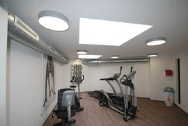 Ein moderner Fitnessraum mit mehreren Trainingsgeräten und hellem Licht, das durch ein großes Oberlicht strömt.
