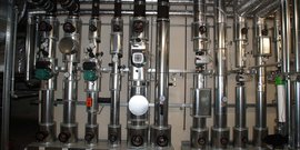 Eine komplexe Anordnung von Metallrohren und Ventilen, die in einem technischen Raum installiert sind, zeigt präzise Messinstrumente.