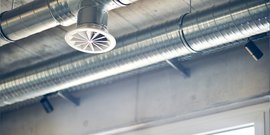 Ein elegantes Lüftungssystem mit einem runden Auslass und glänzenden Rohren, das an einer minimalistischen Decke angebracht ist.