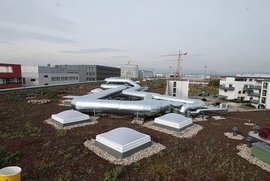 Eine moderne Dachlandschaft mit silbernen Rohren, die sich über ein begrüntes Dach schlängeln, umgeben von Gebäuden.