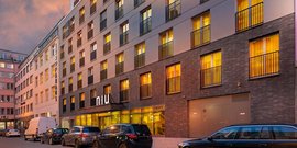 Die Fassade eines stilvollen Hotels mit warmem Licht, das durch die Fenster strahlt, umgeben von parkenden Autos.