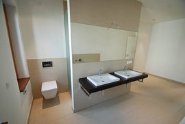 Der Raum zeigt ein helles Badezimmer mit einem WC und zwei stilvollen Waschbecken auf einer dunklen Holzablage.