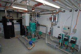 In einem industriellen Umfeld sind grüne Pumpen und Metallrohre sichtbar, die eine komplexe Wasserverteilung darstellen.