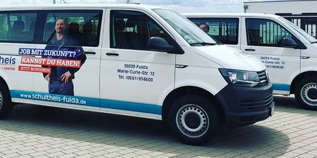 Zwei Lieferwagen mit Werbung für Schulthais stehen auf einem gepflasterten Parkplatz in Fulda, umgeben von Grünflächen.
