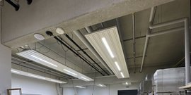Die Decke eines modernen Raumes mit mehreren LED-Leuchten und sichtbaren Rohren, die eine industrielle Atmosphäre schaffen.