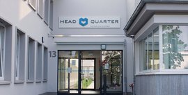 Der Eingang eines modernen Gebäudes mit dem Schriftzug 'HEAD QUARTER' und der Nummer 13 an der Wand.