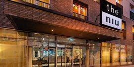 Die moderne Fassade des Hotels 'the niu' mit großen Fenstern und einem einladenden Eingangsbereich bei Dämmerung.