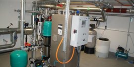 Ein industrieller Raum mit einem großen Druckbehälter, Pumpen und einem Steuerpanel, das die Betriebsparameter überwacht.