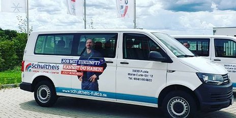 Schultheis Transporter präsentiert Zukunftsperspektiven in Fulda Ein moderner Transporter mit Werbung für Schultheis steht auf einem gepflasterten Parkplatz unter einem bewölkten Himmel.