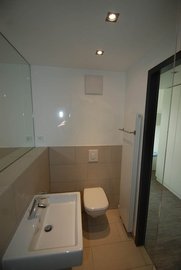 Ein modernes Badezimmer mit einem weißen Waschbecken und einer Toilette, umgeben von hellen Fliesen und einem großen Spiegel.